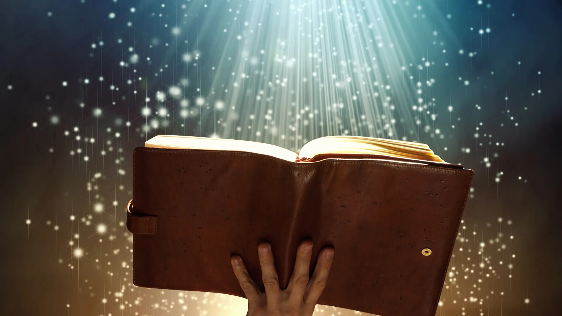univers-narratif Une main tient un livre ouvert sous une lumière scintillante, symbolisant un univers narratif.