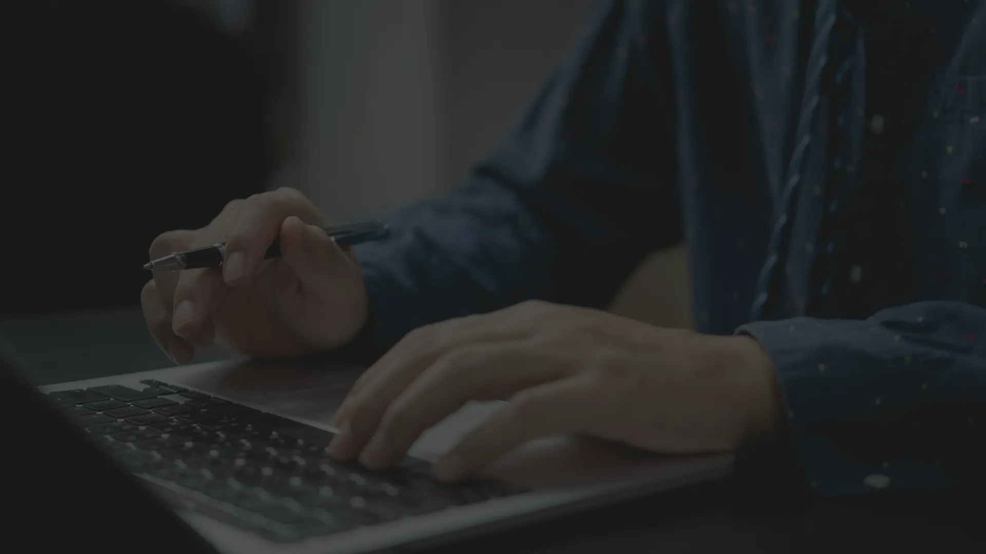Un homme écrit sur les touches de son clavier d'ordinateur un exemple transmédia, un stylo à la main.